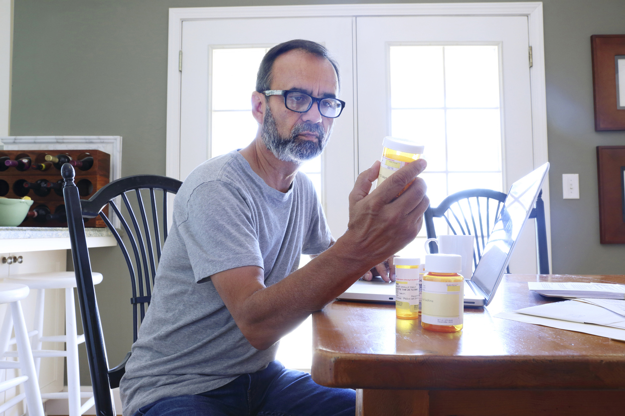 Hispanic Man Sitting At Dining Room Table Looking At His Prescription Medications